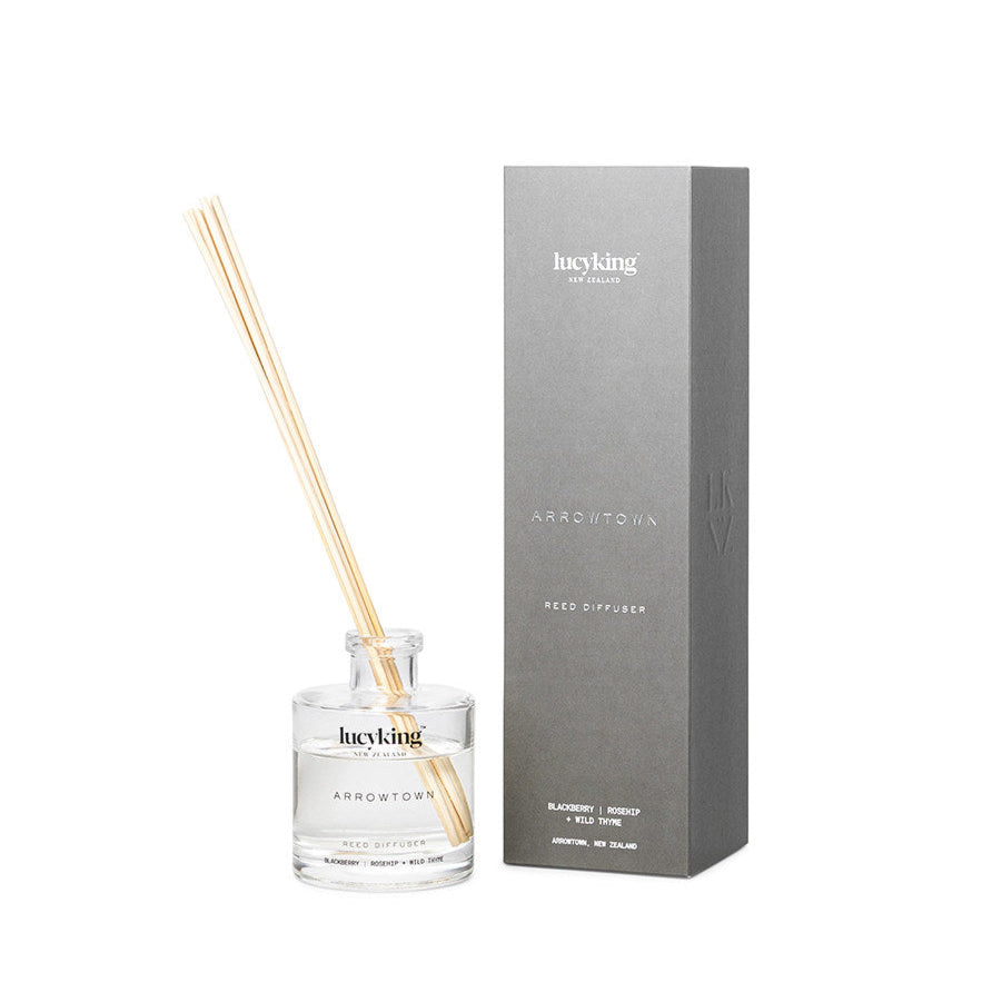 LucyKing ARROWTOWN reed diffuser in clear bottle with beige reeds and grey packaging on a white background